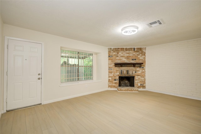 12803 High Star Dr, Houston, TX 77072 - unfurnished living room with light wood-style flooring, a textured ceiling, a brick fireplace, and brick wall