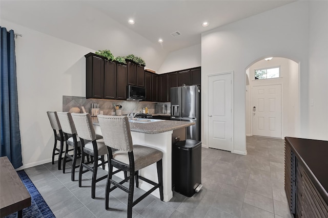 15023 Winter Valley Ct, Humble, TX 77396 - kitchen featuring stainless steel fridge, black microwave, arched walkways, a peninsula, and backsplash