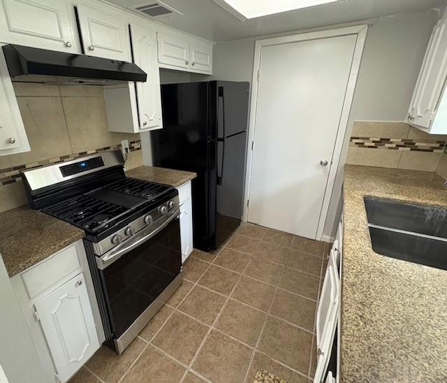 12127 Rhinebeck Dr, Houston, TX 77089 - kitchen featuring stainless steel gas range oven, under cabinet range hood, backsplash, white cabinetry, and freestanding refrigerator