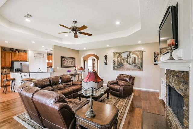 29218 Hay Meadow Ct, Waller, TX 77484 - living area featuring a tray ceiling, arched walkways, ceiling fan, a fireplace, and light wood finished floors