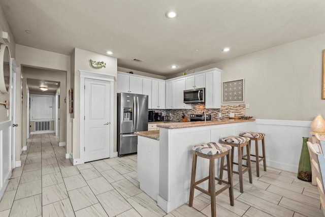 4121 Pointe W Dr Unit 103, Galveston, TX 77554 - kitchen featuring appliances with stainless steel finishes, a peninsula, white cabinetry, a kitchen breakfast bar, and backsplash