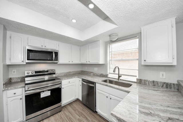17715 Glenpatti Dr, Houston, TX 77084 - kitchen with stainless steel appliances, a textured ceiling, white cabinets, light wood-style floors, and tasteful backsplash