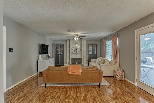100 W Rainbow Ridge Cir, The Woodlands, TX 77381 - living room with light wood-style floors, a fireplace, a textured ceiling, and a ceiling fan