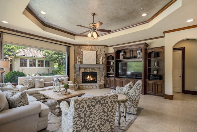 102 Lake Sterling Gate Dr, Spring, TX 77379 - living area with a tray ceiling, ceiling fan, a stone fireplace, ornamental molding, and arched walkways