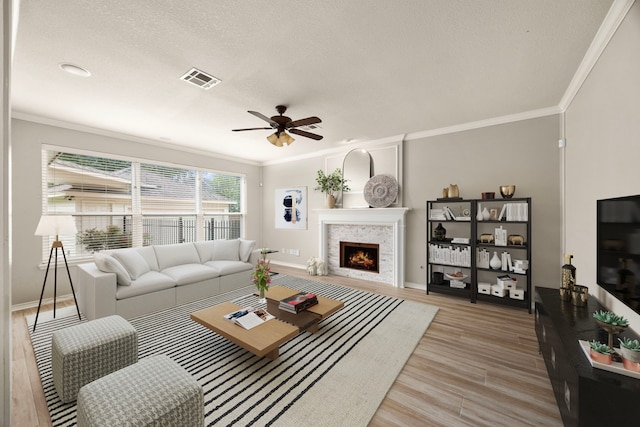 22 Windfern Pl, The Woodlands, TX 77382 - living room featuring a ceiling fan, ornamental molding, light wood finished floors, a warm lit fireplace, and a textured ceiling