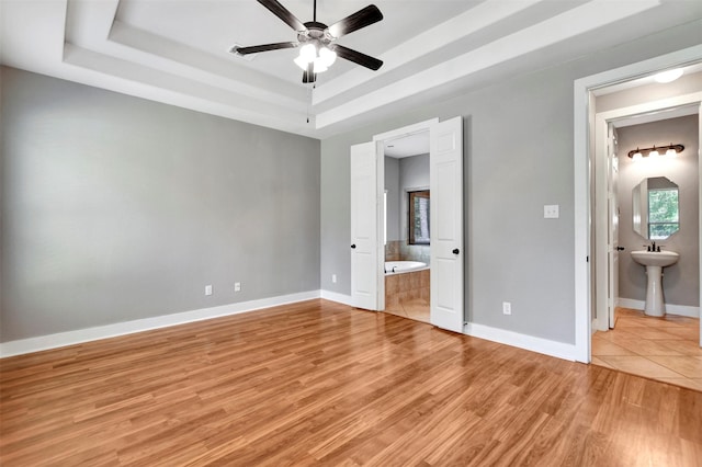 59 Beaconsfield Dr, Magnolia, TX 77355 - unfurnished bedroom featuring a tray ceiling, ensuite bath, and light wood-type flooring