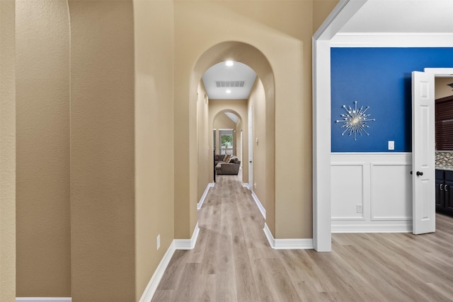 100 Anderson Ranch Ln, Friendswood, TX 77546 - hallway featuring arched walkways, light wood-style flooring, a wainscoted wall, and a decorative wall