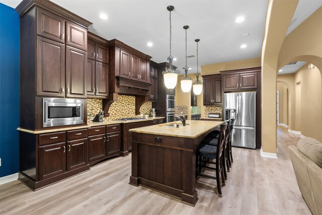 100 Anderson Ranch Ln, Friendswood, TX 77546 - kitchen with appliances with stainless steel finishes, arched walkways, decorative backsplash, light wood-style floors, and dark brown cabinetry