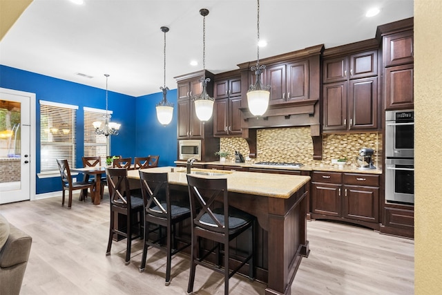 100 Anderson Ranch Ln, Friendswood, TX 77546 - kitchen featuring appliances with stainless steel finishes, light wood finished floors, tasteful backsplash, a center island with sink, and recessed lighting