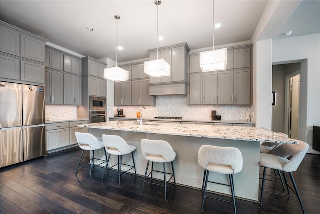34207 Mill Creek Ct, Pinehurst, TX 77362 - kitchen with appliances with stainless steel finishes, gray cabinetry, decorative backsplash, light stone countertops, and a large island