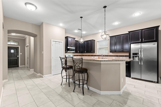 19647 Travis Cannon Ln, Richmond, TX 77407 - kitchen featuring appliances with stainless steel finishes, arched walkways, a breakfast bar, light stone counters, and a center island