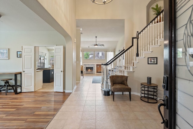 23 Murmuring Creek Pl, The Woodlands, TX 77385 - entrance foyer featuring a warm lit fireplace, ceiling fan, stairs, a high ceiling, and wood finished floors