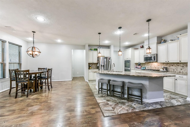 10147 Cimarron Canyon Ln, Magnolia, TX 77354 - kitchen featuring appliances with stainless steel finishes, backsplash, a kitchen island with sink, wood-type flooring, and a kitchen breakfast bar