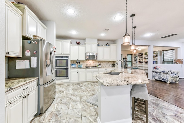 10147 Cimarron Canyon Ln, Magnolia, TX 77354 - kitchen featuring appliances with stainless steel finishes, white cabinetry, hanging light fixtures, light stone counters, and a breakfast bar area