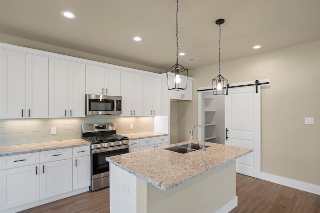 735 20th St, Hempstead, TX 77445 - kitchen with appliances with stainless steel finishes, dark wood-style floors, a barn door, white cabinetry, and backsplash