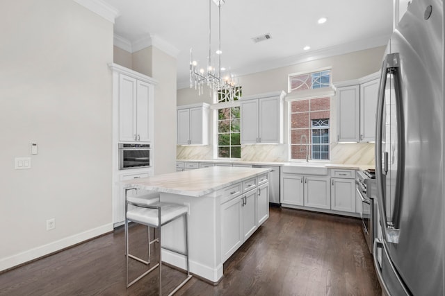 1801 Ashland St, Houston, TX 77008 - kitchen with stainless steel appliances, decorative backsplash, a chandelier, white cabinets, and ornamental molding