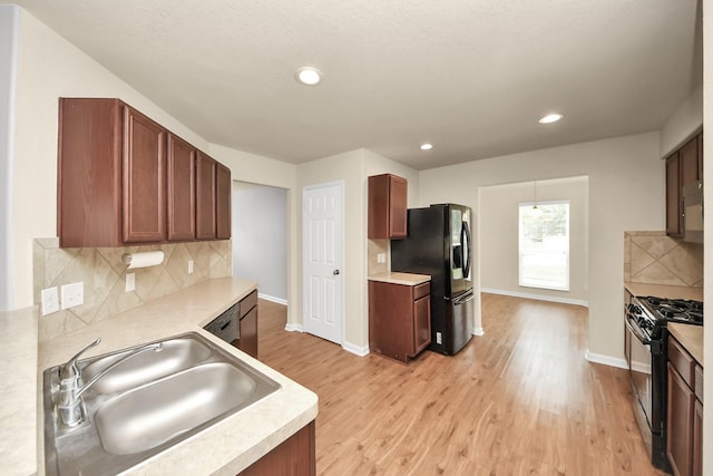 9914 Swallow Dr, Conroe, TX 77385 - kitchen with gas stove, black fridge with ice dispenser, light countertops, decorative backsplash, and light wood-type flooring