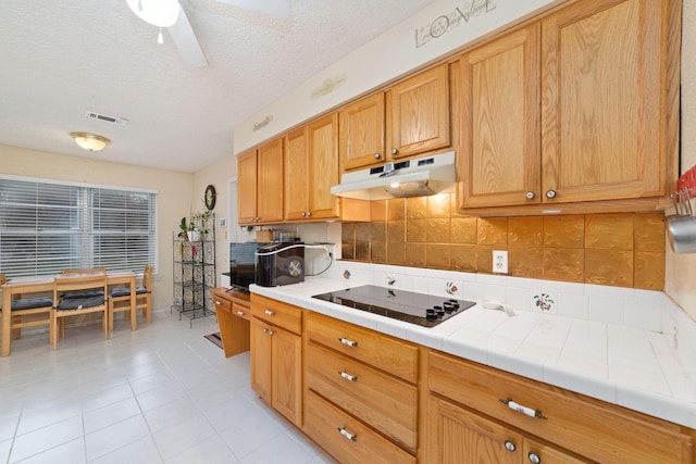 12611 Bexhill Dr, Houston, TX 77065 - kitchen with under cabinet range hood, black electric stovetop, a textured ceiling, light tile patterned flooring, and tile counters