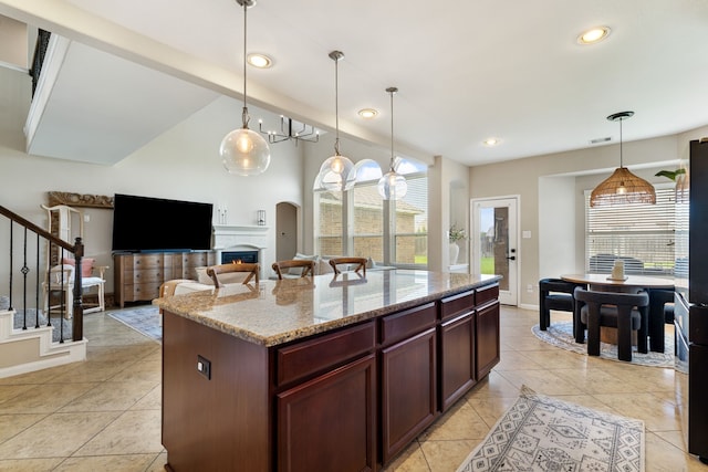 20314 Tarpon Bay Ln, Cypress, TX 77433 - kitchen featuring light stone counters, a center island, pendant lighting, light tile patterned flooring, and a warm lit fireplace
