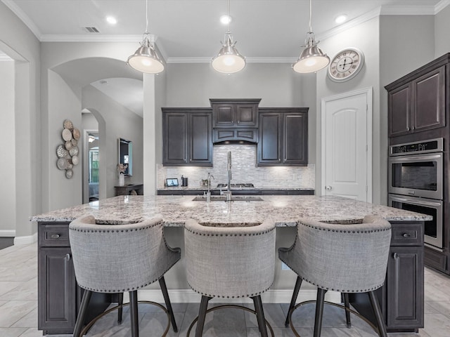 4623 Bisontine Bay Ln, Rosharon, TX 77583 - kitchen with stainless steel appliances, arched walkways, light stone countertops, a kitchen breakfast bar, and ornamental molding