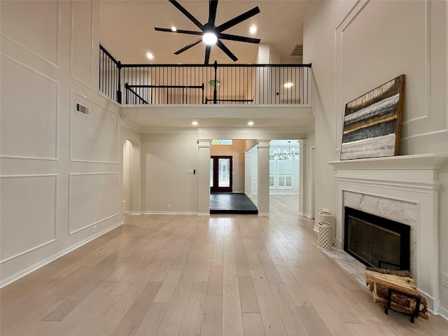19 Pebble Hollow Ct, The Woodlands, TX 77381 - unfurnished living room with a ceiling fan, a high end fireplace, a high ceiling, light wood finished floors, and decorative columns