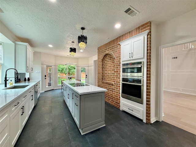 19 Pebble Hollow Ct, The Woodlands, TX 77381 - kitchen with stainless steel appliances, white cabinetry, a kitchen island, decorative light fixtures, and light stone countertops