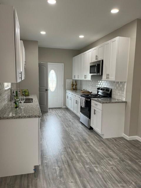 1012 Rd 5606, Cleveland, TX 77327 - kitchen with appliances with stainless steel finishes, white cabinetry, wood finished floors, backsplash, and recessed lighting