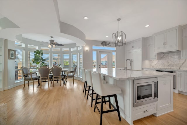 1303 Outrigger, Tiki Island, TX 77554 - kitchen featuring stainless steel microwave, ceiling fan, light wood-style flooring, a kitchen island with sink, and light stone counters