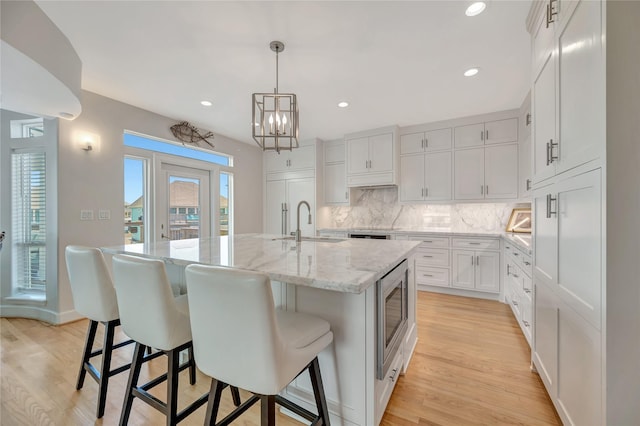 1303 Outrigger, Tiki Island, TX 77554 - kitchen with stainless steel microwave, backsplash, an island with sink, light wood-style floors, and a breakfast bar area