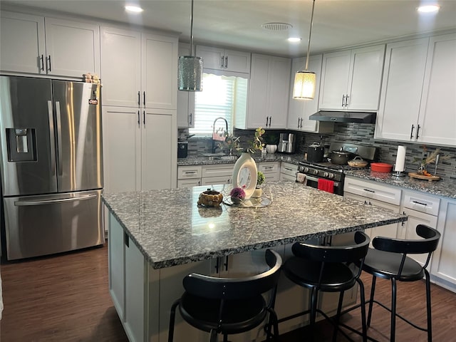 8823 Shadow Crest St, Houston, TX 77074 - kitchen with stainless steel appliances, under cabinet range hood, dark wood-style floors, dark stone counters, and decorative backsplash