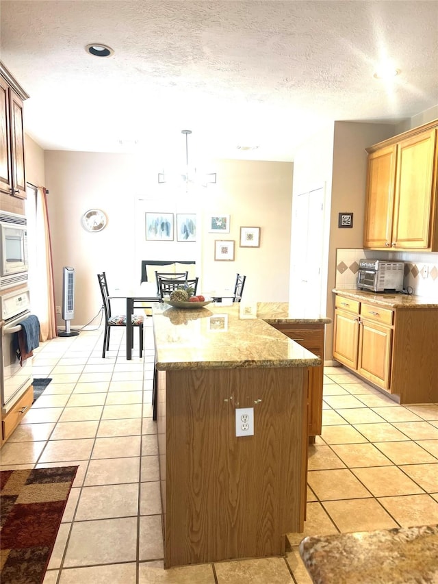 15415 Longhorn Cavern Dr, Sugar Land, TX 77498 - kitchen with oven, built in microwave, a kitchen island, light tile patterned floors, and light stone counters