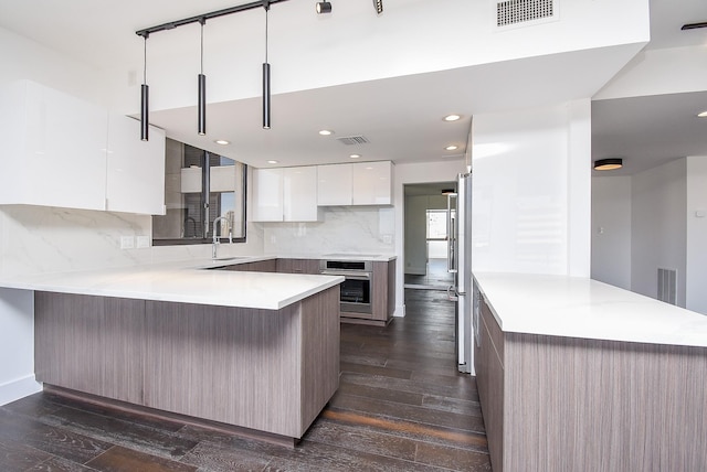 49 Briar Hollow Ln Unit 1106, Houston, TX 77027 - kitchen with modern cabinets, a peninsula, stainless steel appliances, dark wood finished floors, and backsplash
