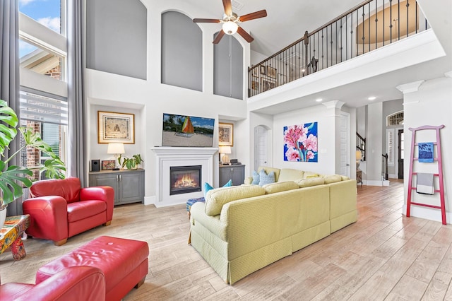 32647 Turning Springs Dr, Fulshear, TX 77423 - living area with a high ceiling, a ceiling fan, a glass covered fireplace, wood finished floors, and decorative columns