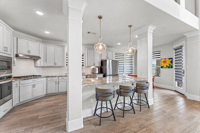 32647 Turning Springs Dr, Fulshear, TX 77423 - kitchen with stainless steel appliances, decorative columns, light wood-type flooring, tasteful backsplash, and light stone countertops