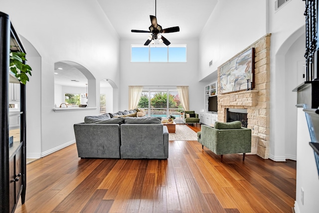 12702 Eagle Ledge Ln, Tomball, TX 77377 - living room featuring a ceiling fan, a stone fireplace, hardwood / wood-style flooring, a high ceiling, and arched walkways