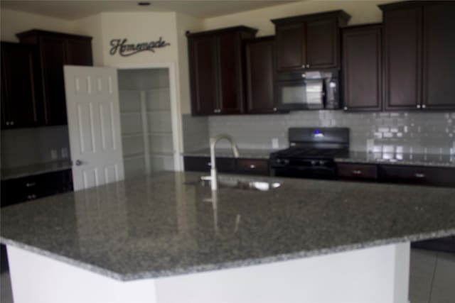 26350 Riley Glen Dr, Richmond, TX 77406 - kitchen with black microwave, stove, decorative backsplash, dark stone countertops, and a large island with sink