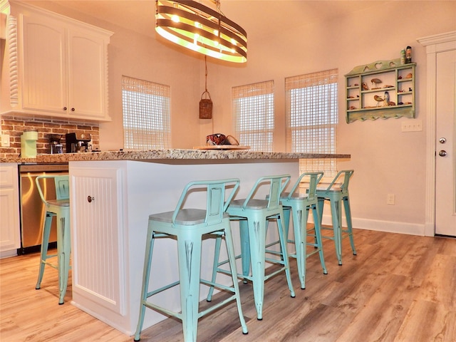 110 Pelican Pl, Surfside Beach, TX 77541 - kitchen with stainless steel dishwasher, light wood-type flooring, white cabinetry, a kitchen breakfast bar, and backsplash