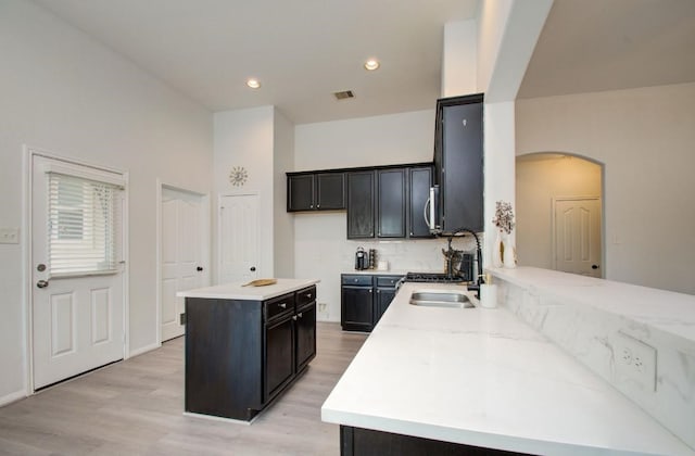 17603 Memorial Falls Dr, Tomball, TX 77375 - kitchen with arched walkways, backsplash, light wood-style floors, stainless steel microwave, and a kitchen island