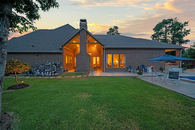 30 Madrone Terrace Pl, Tomball, TX 77375 - back of property at dusk featuring a chimney, a patio, brick siding, and a lawn