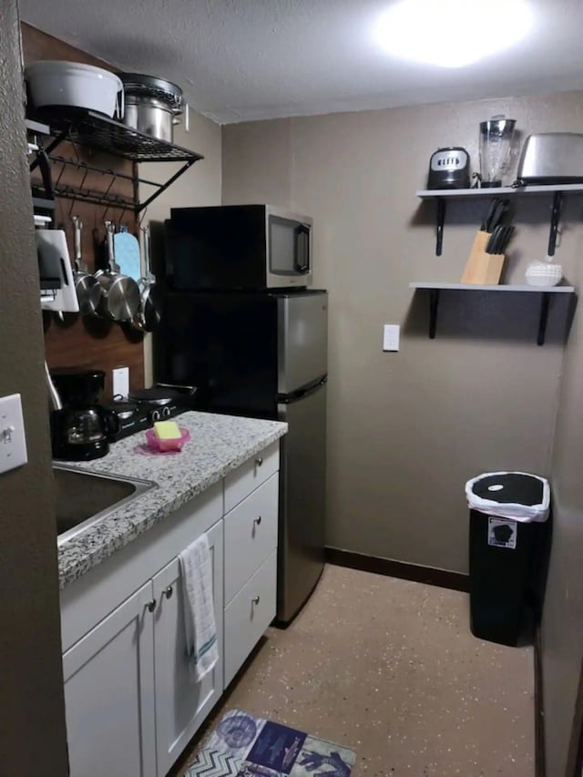 23002 Vida, Galveston, TX 77554 - kitchen with white cabinetry, open shelves, freestanding refrigerator, a textured ceiling, and light stone countertops