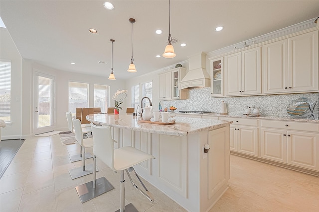 47 Monarch Trl, Sugar Land, TX 77498 - kitchen featuring premium range hood, backsplash, light stone countertops, an island with sink, and light tile patterned flooring