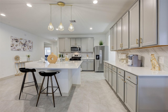 29918 Reagans Ranch Dr, Katy, TX 77494 - kitchen with appliances with stainless steel finishes, gray cabinets, decorative backsplash, a breakfast bar area, and an island with sink
