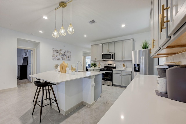 29918 Reagans Ranch Dr, Katy, TX 77494 - kitchen with stainless steel appliances, gray cabinetry, a kitchen bar, backsplash, and light countertops