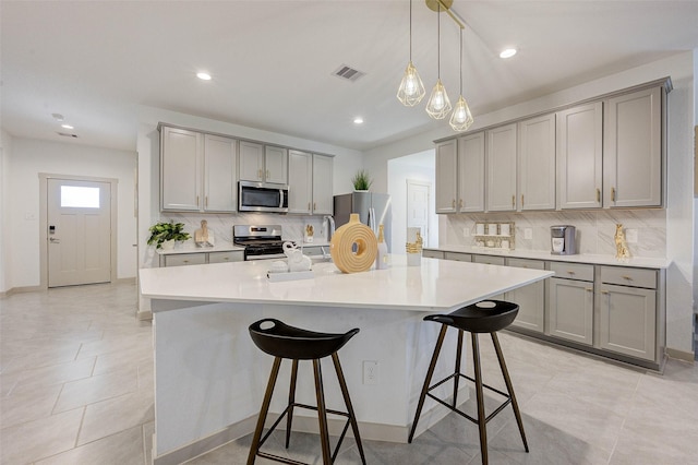 29918 Reagans Ranch Dr, Katy, TX 77494 - kitchen featuring gray cabinets, appliances with stainless steel finishes, a kitchen breakfast bar, decorative backsplash, and recessed lighting