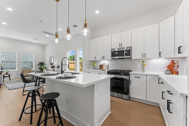 8302 Springwood Canyon Ln, Houston, TX 77055 - kitchen featuring stainless steel appliances, a center island with sink, tasteful backsplash, light wood-style floors, and light countertops