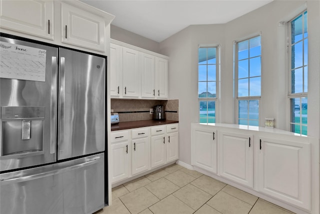 9826 Palm Dr, Mont Belvieu, TX 77523 - kitchen featuring stainless steel refrigerator with ice dispenser, tasteful backsplash, dark countertops, light tile patterned floors, and white cabinets