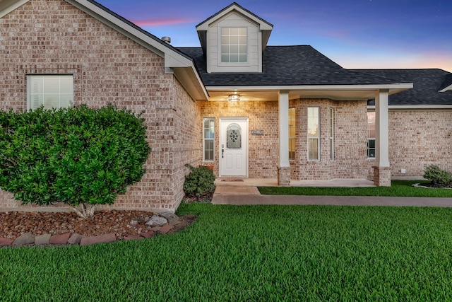 9826 Palm Dr, Mont Belvieu, TX 77523 - exterior entry at dusk featuring brick siding, a yard, and a shingled roof