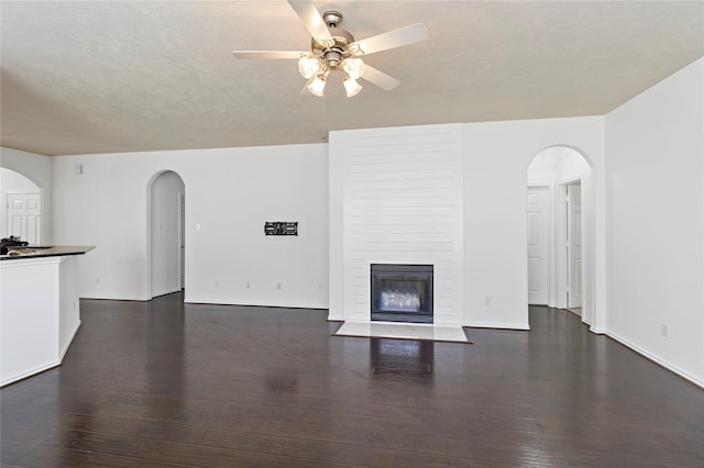23307 W Pine Ivy Ln, Tomball, TX 77375 - unfurnished living room featuring arched walkways, a ceiling fan, a large fireplace, and hardwood / wood-style floors