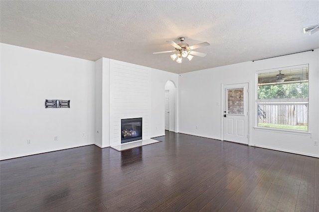 23307 W Pine Ivy Ln, Tomball, TX 77375 - unfurnished living room featuring arched walkways, a ceiling fan, dark wood-style floors, a large fireplace, and a textured ceiling