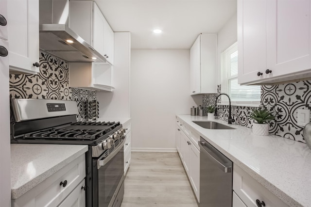 4330 Heite St, Houston, TX 77022 - kitchen featuring appliances with stainless steel finishes, wall chimney range hood, light wood-type flooring, tasteful backsplash, and white cabinetry